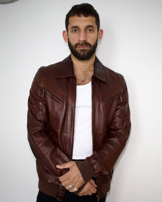 Man wearing a brown leather just cavalli jacket over a white shirt against a plain background