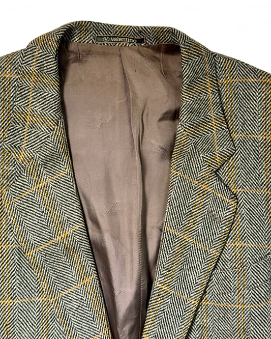 Close-up of a men's valentino herringbone tweed blazer in gray and brown with a thin yellow windowpane check pattern, showing the interior lining.