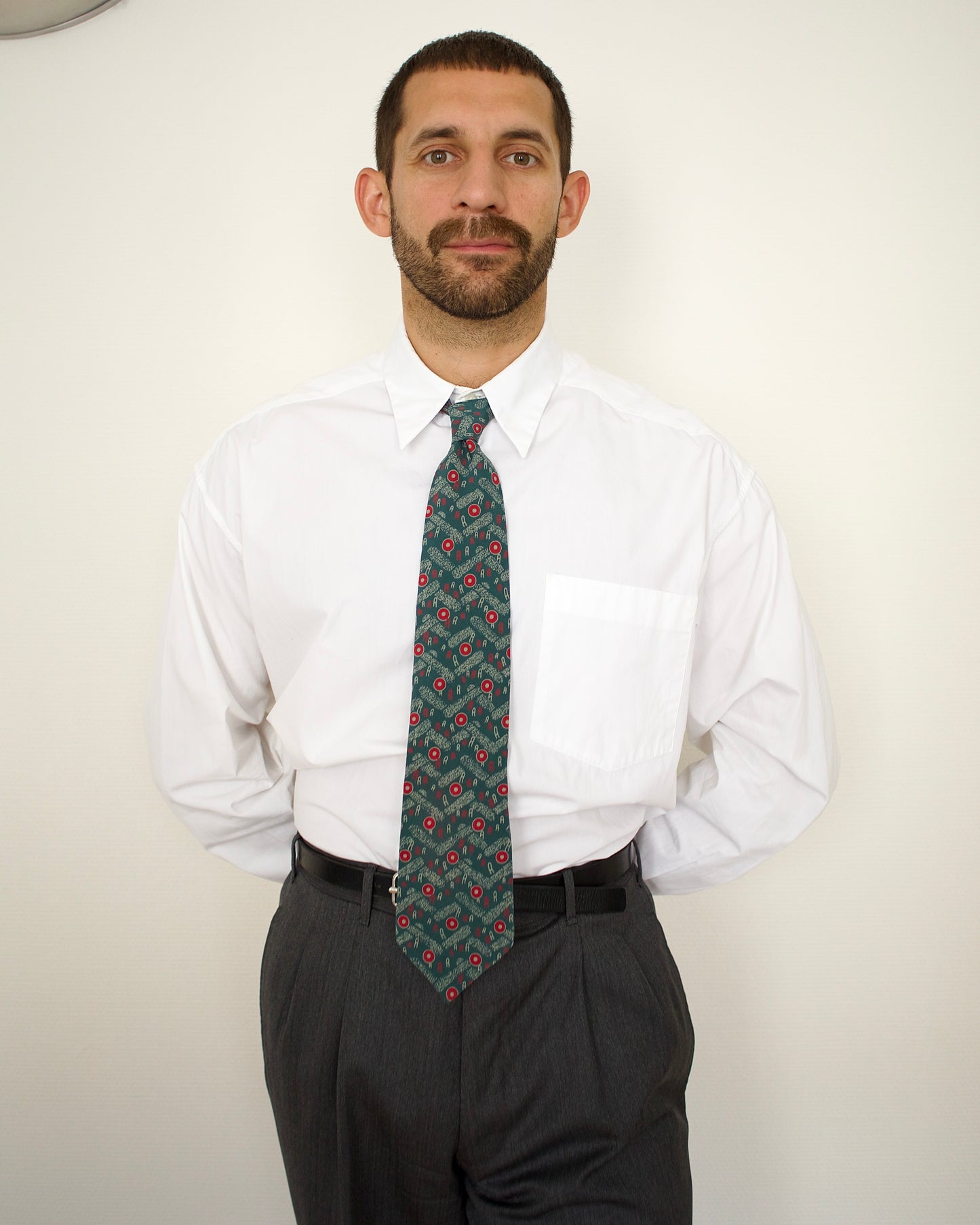Man wearing a white shirt and patterned tie against a plain background