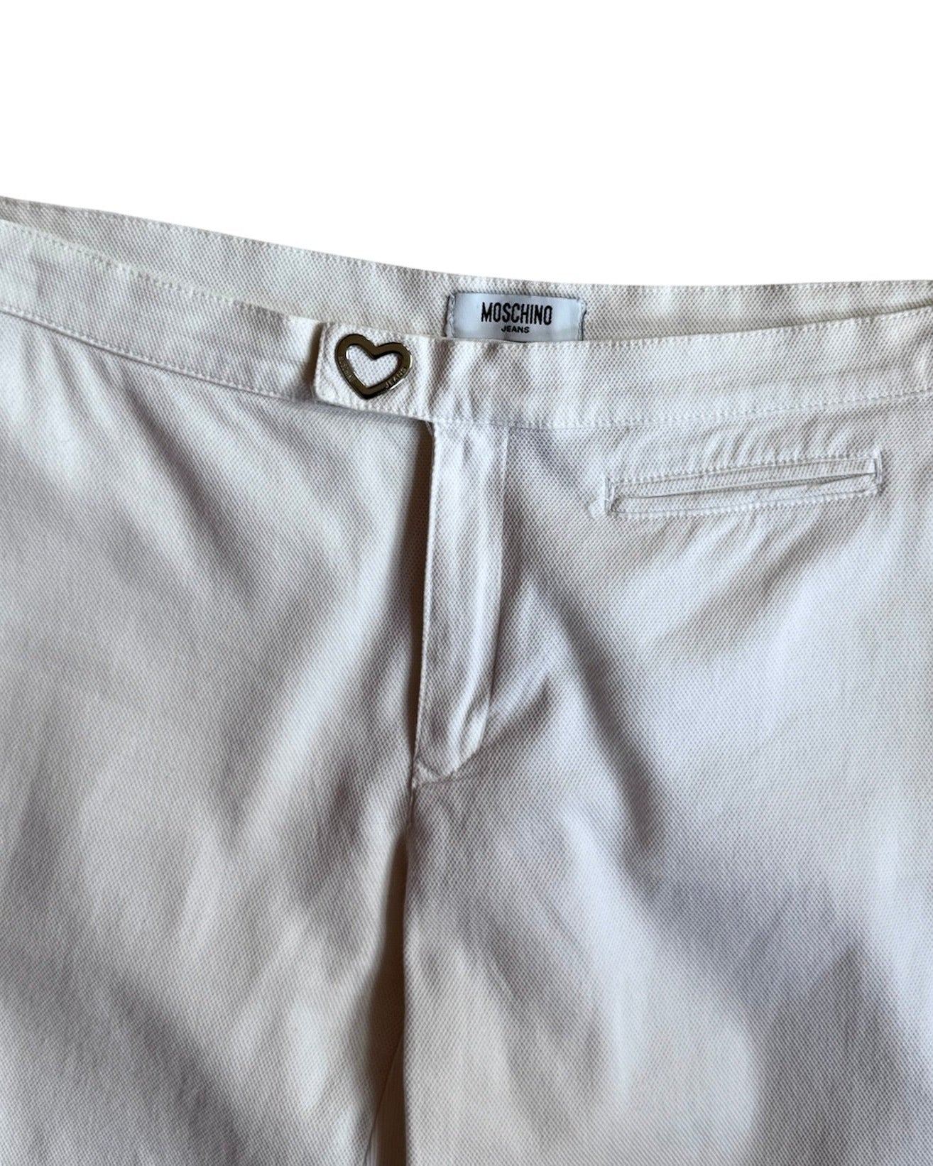 Flat lay of vintage white Moschino pants with heart-shaped button closure, straight leg fit, and mid-rise waist, displayed on a white background.