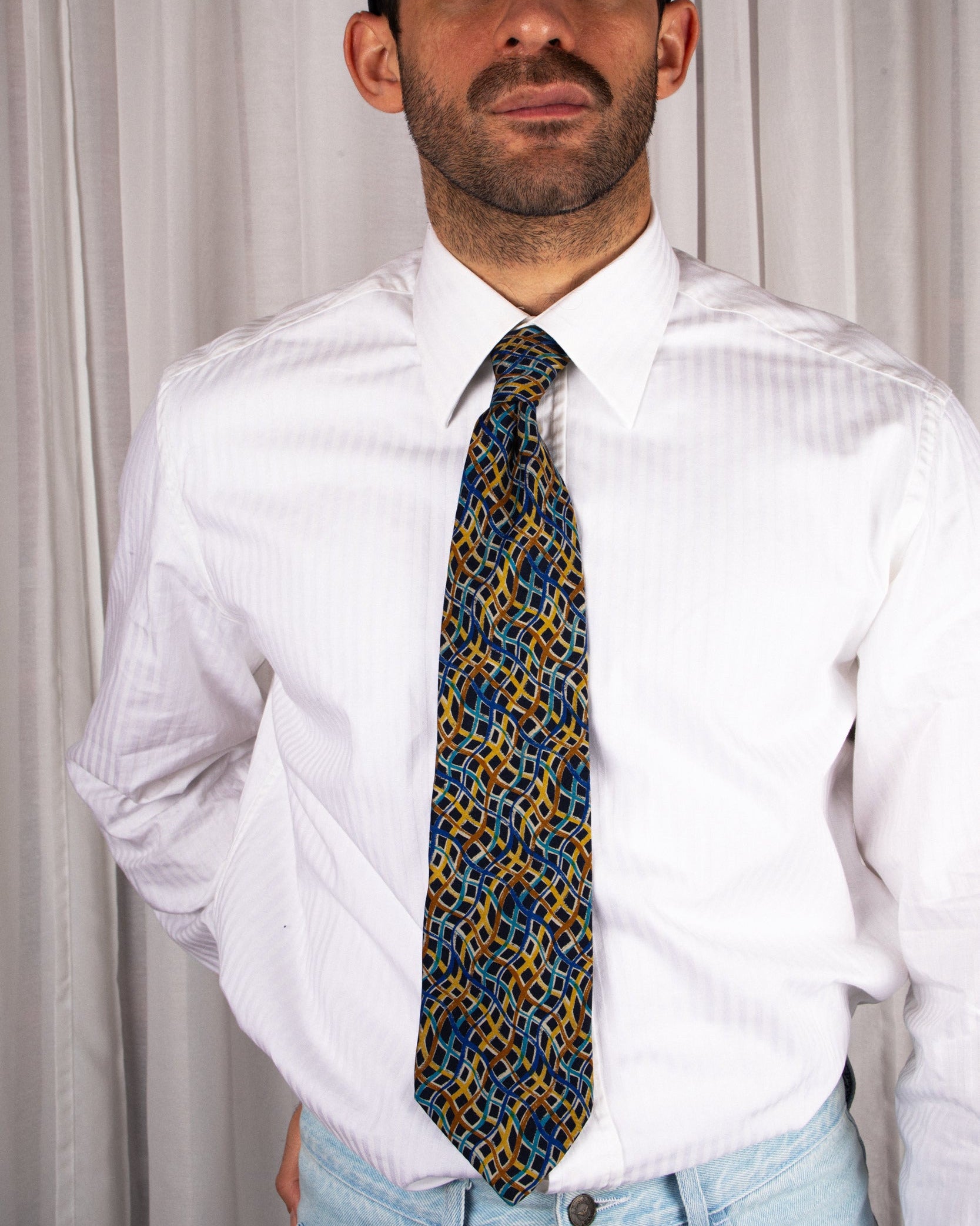 Man wearing a white shirt and patterned tie against a plain background