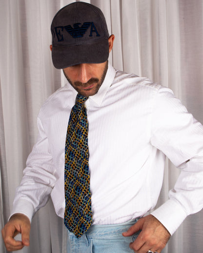Man wearing a white shirt, patterned vintage missoni tie, and dark cap with logo against a plain background