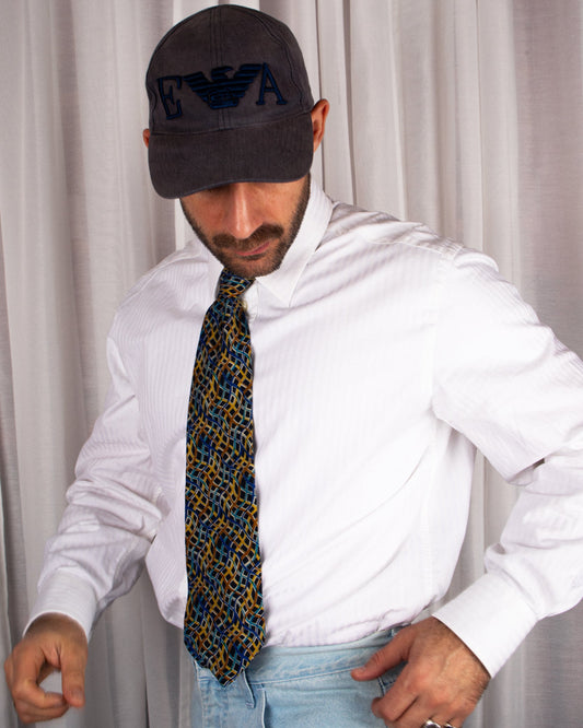 Man wearing a white shirt, patterned vintage missoni tie, and dark cap with logo against a plain background