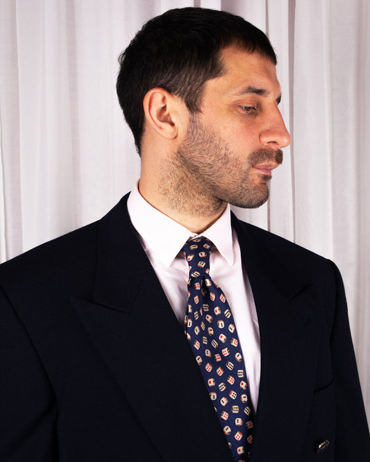 Man wearing a dark suit and patterned gucci tie against a white curtain background