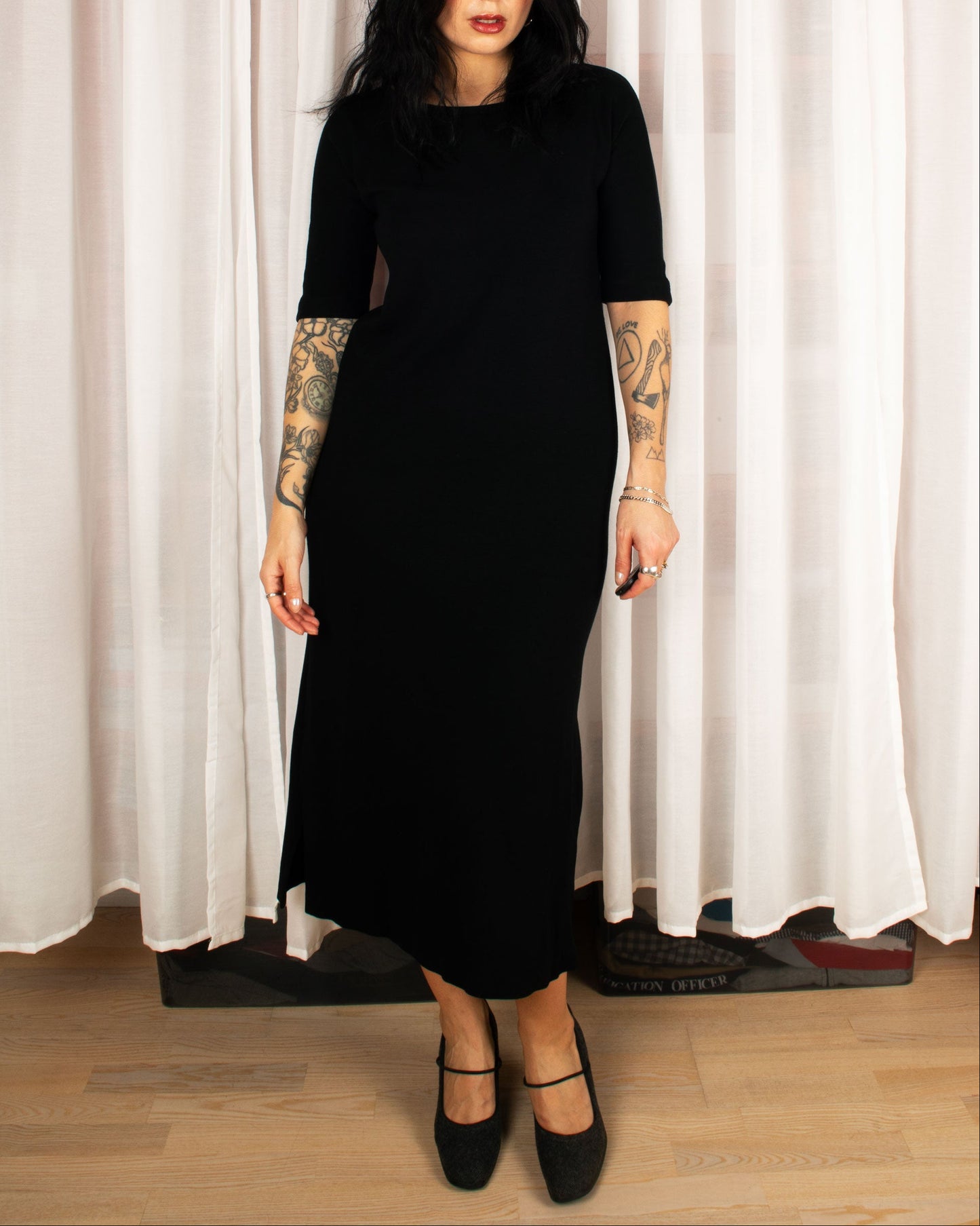 Person wearing a black dress with cut-out design in front of white curtains