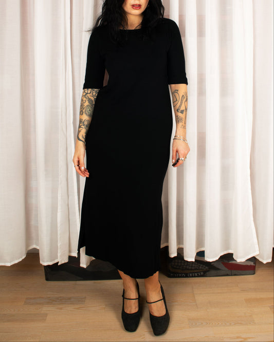 Person wearing a black dress with cut-out design in front of white curtains