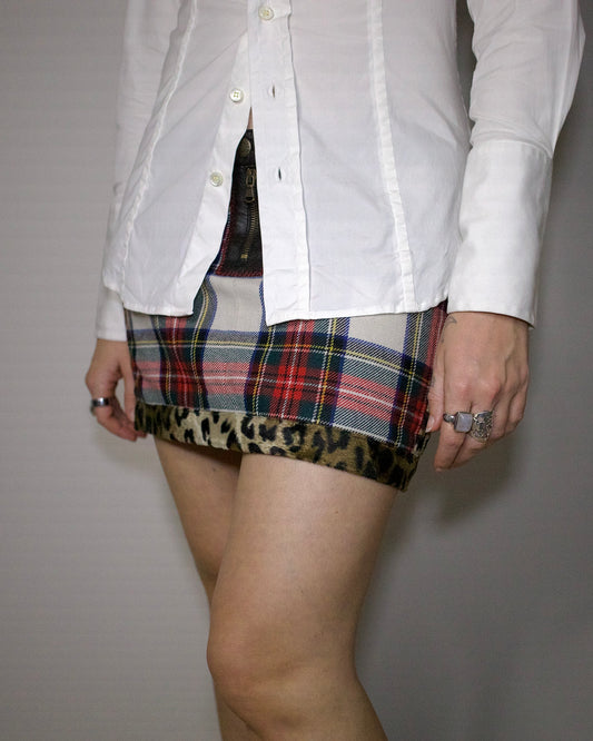 Person wearing a white shirt and Jean Paul Gaultier plaid skirt with leopard print hem on a plain background