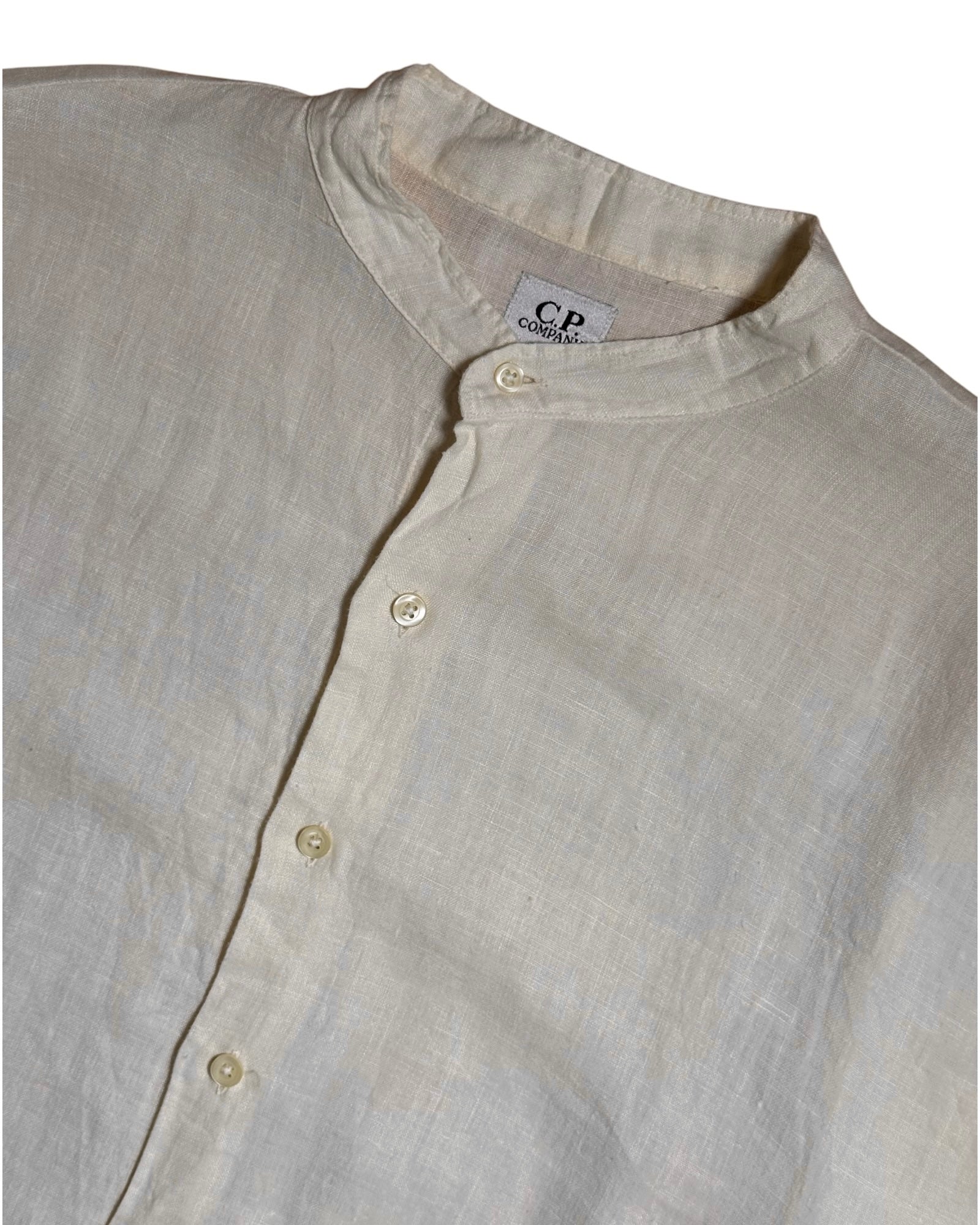 Close-up of a light beige linen shirt with a mandarin collar and button-down front, showing a CP Classics neck label.