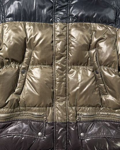 Close-up of a Prada puffer jacket with a color-blocked design, featuring a metallic olive-gold center panel and black and brown sections at the top and bottom.
