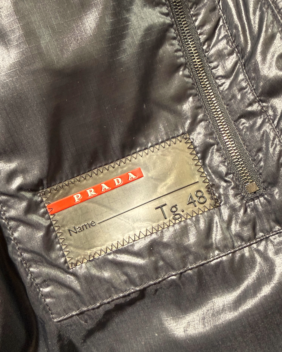 Close-up of a Prada garment interior showing a metallic silver zipper and a sewn-in label with the Prada logo and 'Tg. 48' printed on it.