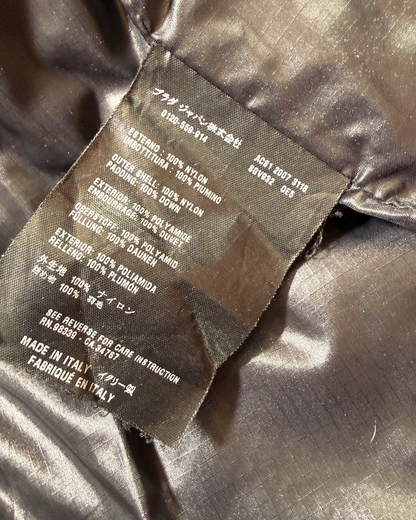 Close-up of a sewn-in product Prada label on shiny dark brown or bronze fabric, showing text including material composition and Made in Italy.