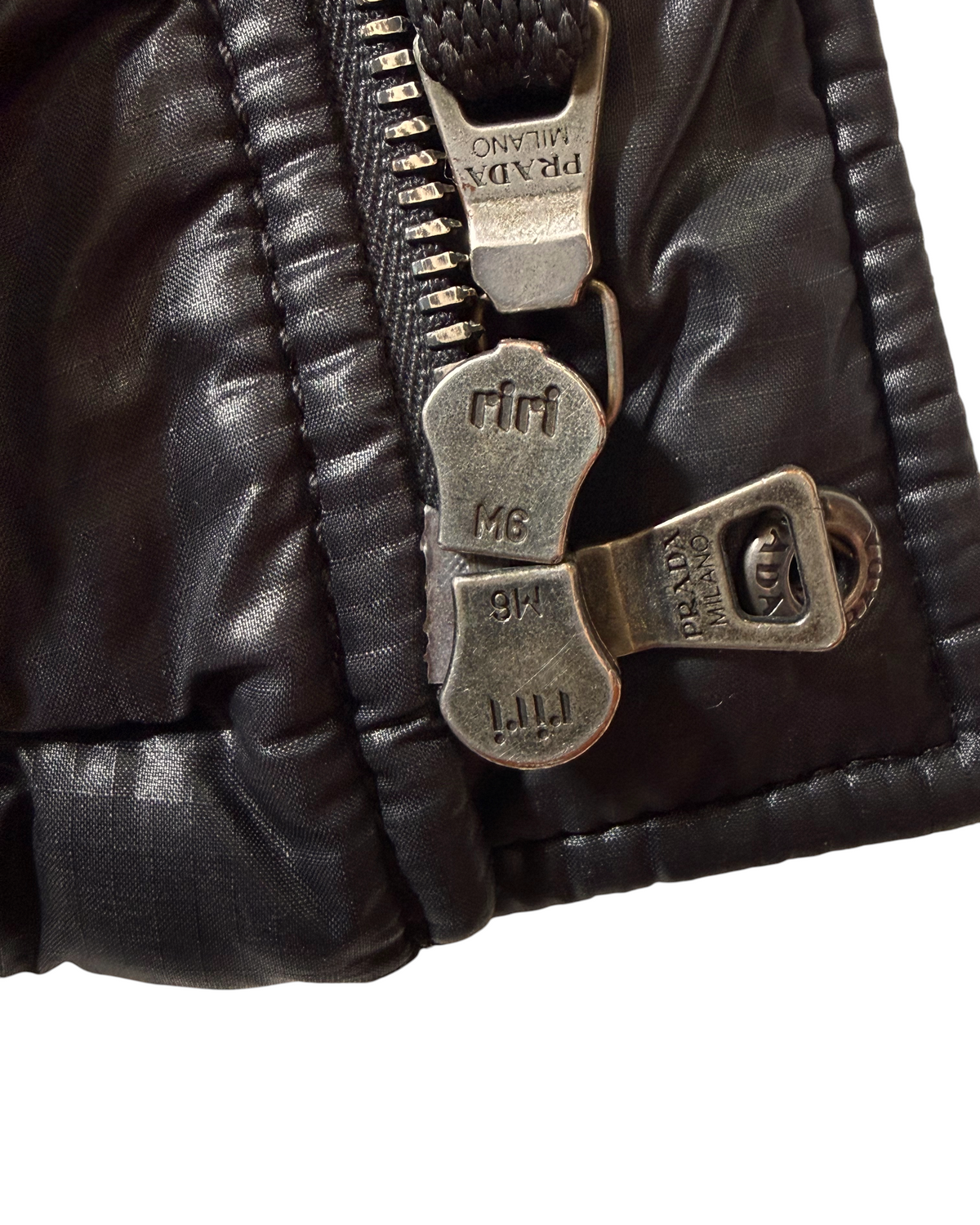 Close-up of a puffer jacket with bronze zipper pulls engraved with 'Prada Milano' and riri.