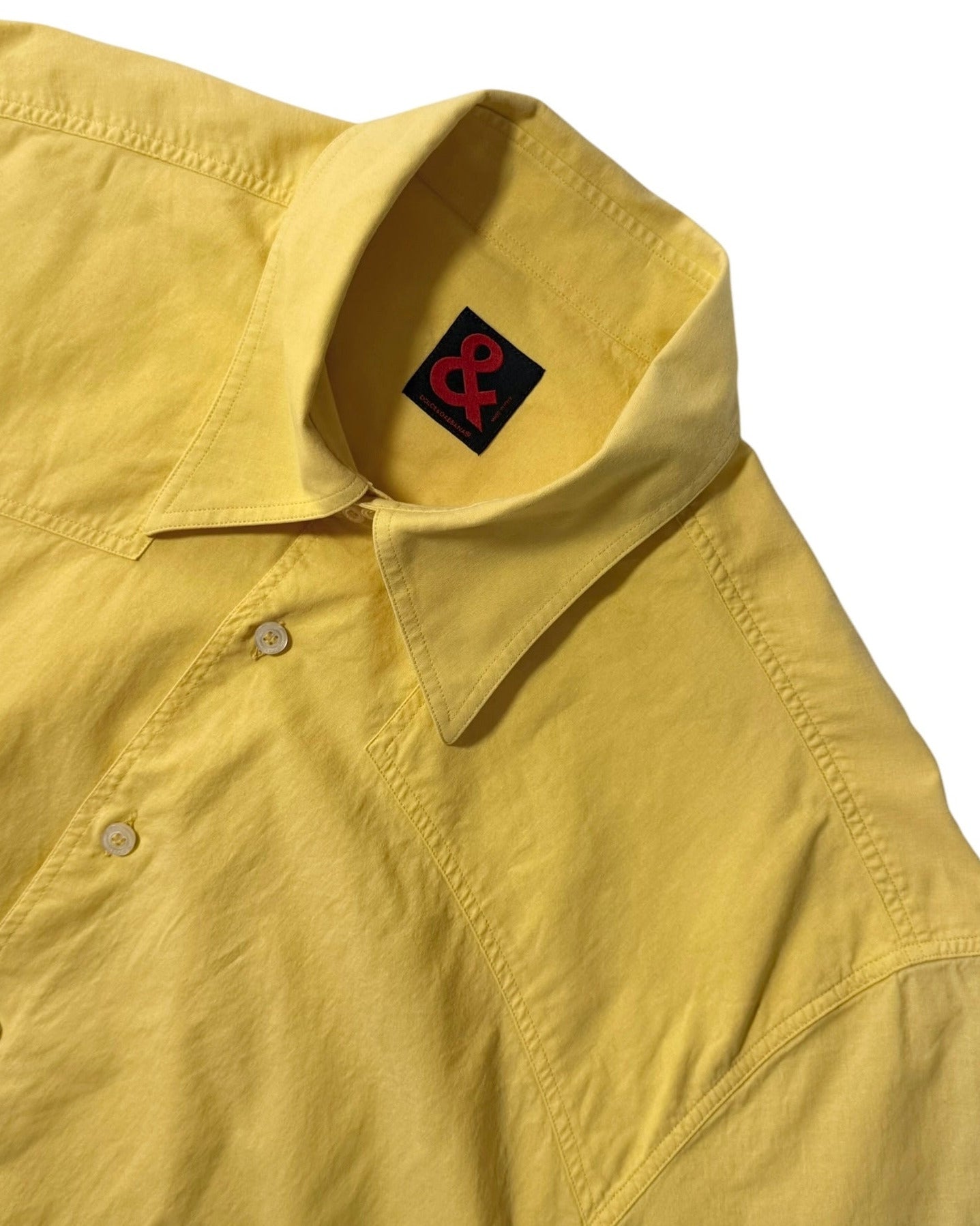Yellow shirt with a Dolce & Gabbana logo patch on the collar against a white background