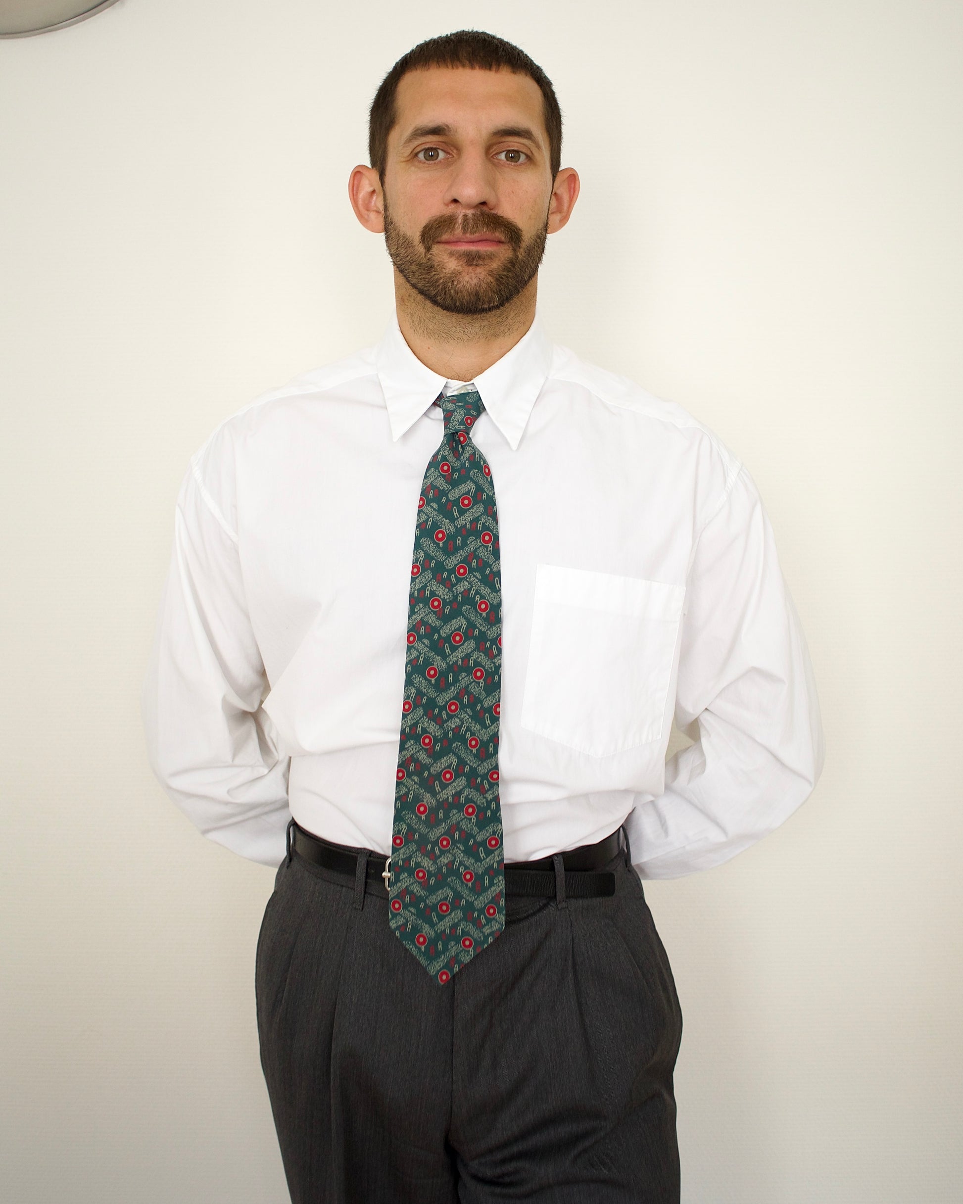 Man wearing a white shirt and patterned tie against a plain background